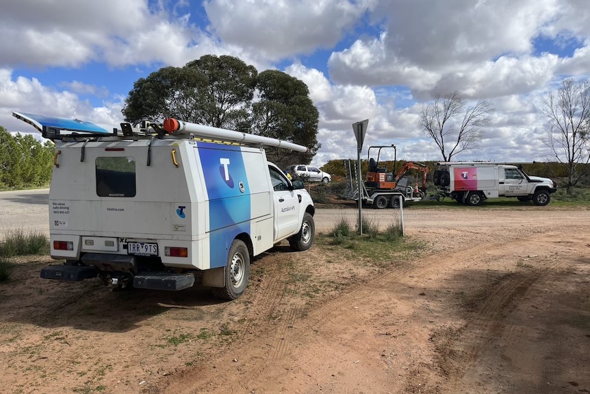 Two Telstra cars on a dirt road.