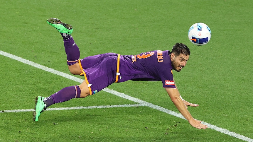 A soccer player wearing purple dives to reach the ball with his head