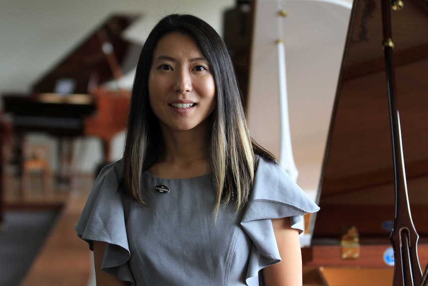 Jenny Ko standing in her family's Gospel Pianos showroom with grand pianos in the background