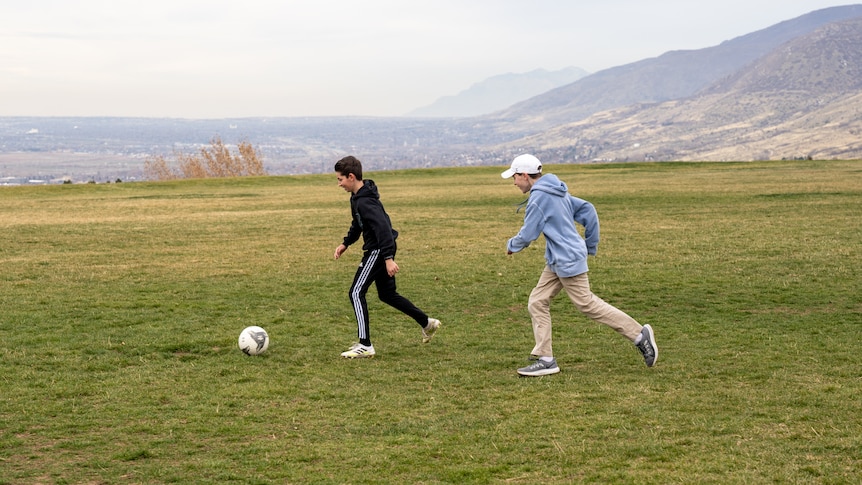 Two boys kick as soccer ball in a field 
