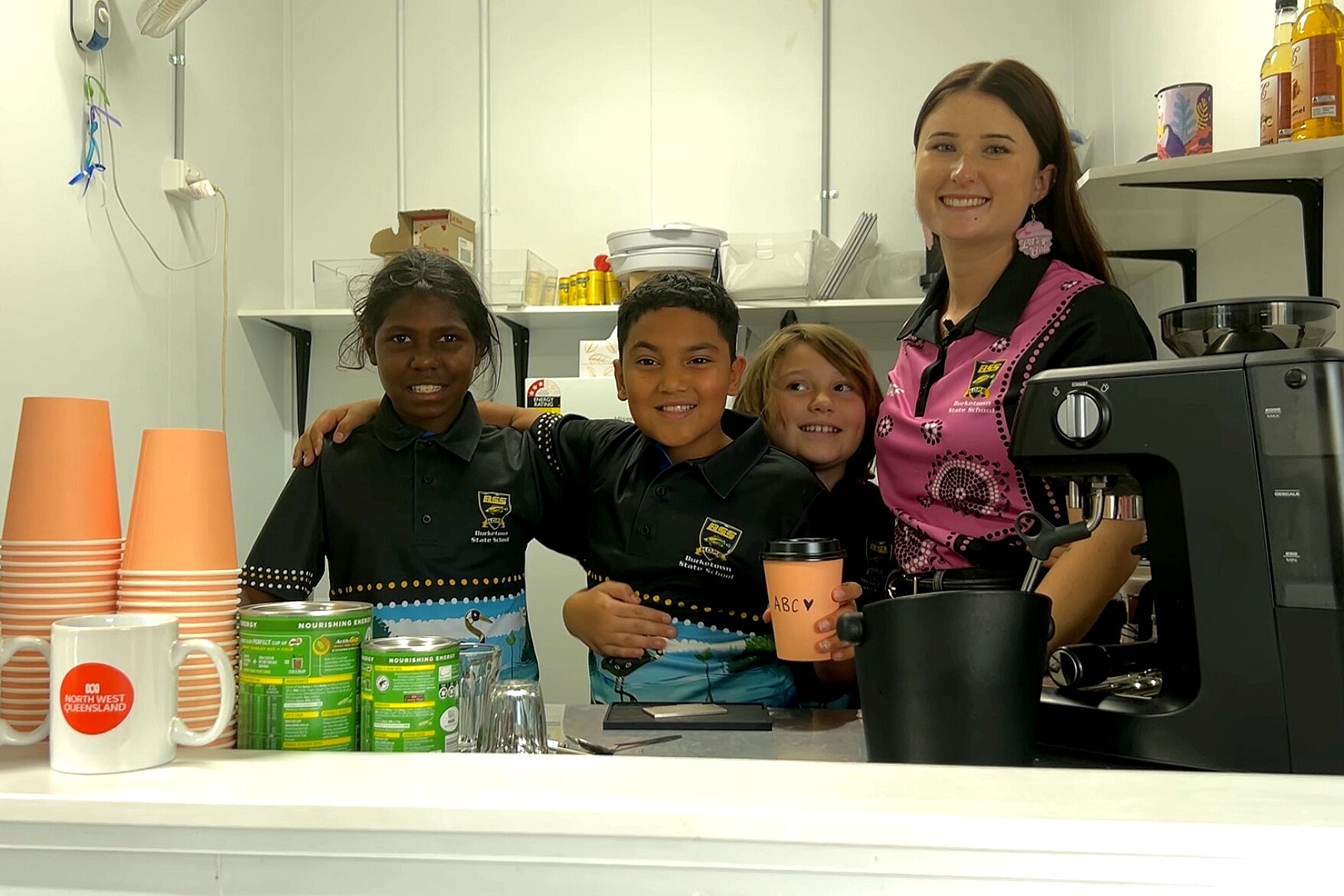Three students and their teacher stand behind a counter.