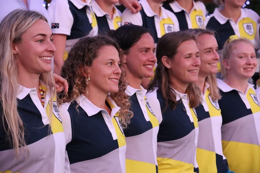 A team of Hockeyroos players smile at the camera. They look excited.