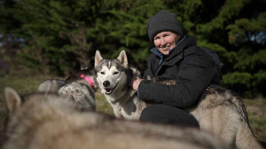 Trish smiles, crouched next to one of her dogs.