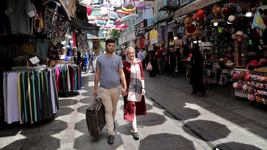 A couple hold hands as they walk through a market place.
