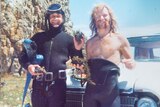 Old photo of two men in wetsuits holding abalones.