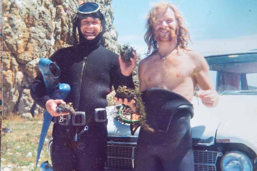 Old photo of two men in wetsuits holding abalones.