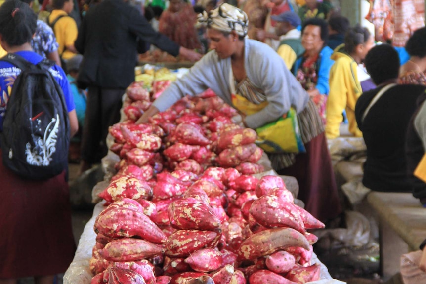 Bright red sweet potatoes in the foreground, while a Papua New Guinea woman sorts them in the background.