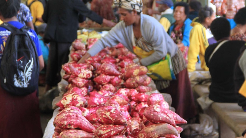 Bright red sweet potatoes in the foreground, while a Papua New Guinea woman sorts them in the background.