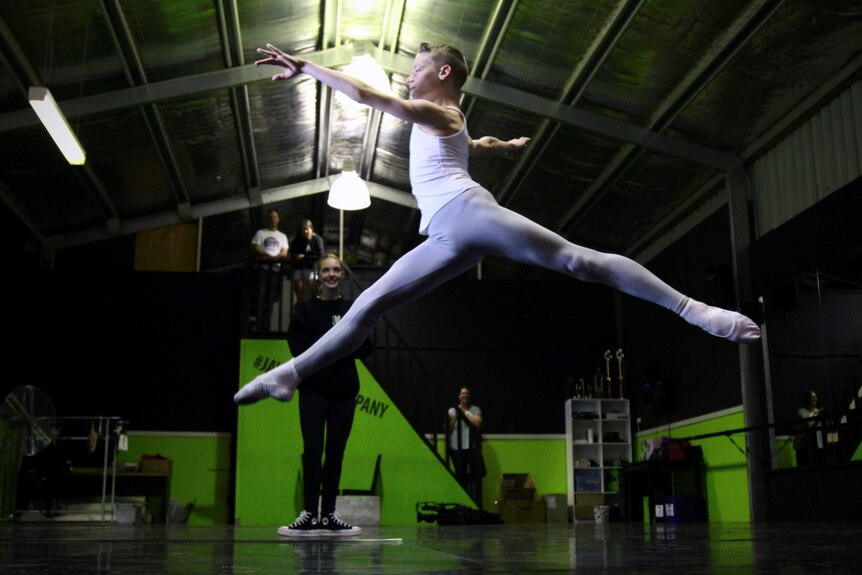 A boy in a ballet outfit leaps across the floor.