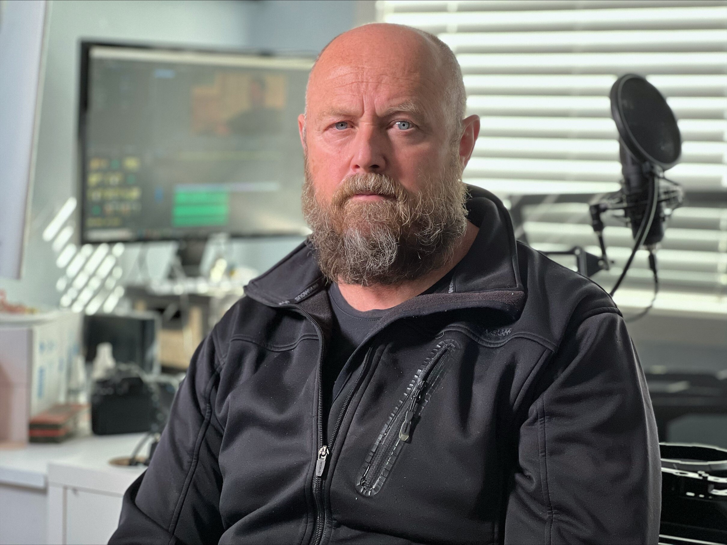 Man wearing black jumper with computer monitor in the background. 