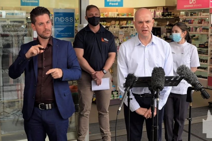 A group of four people including the chief health officer, and a signing interpreter, stand outside a pharmacy.