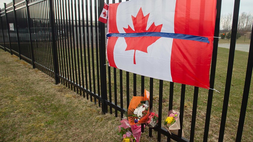 A Canadian flag attached to a fence with flowers.