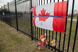 A Canadian flag attached to a fence with flowers.