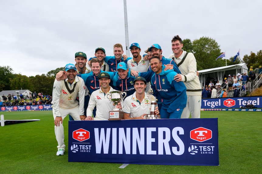 Australia's men's cricket team smile as they stand together for a group shot in front of a banner saying 'Winners'. 