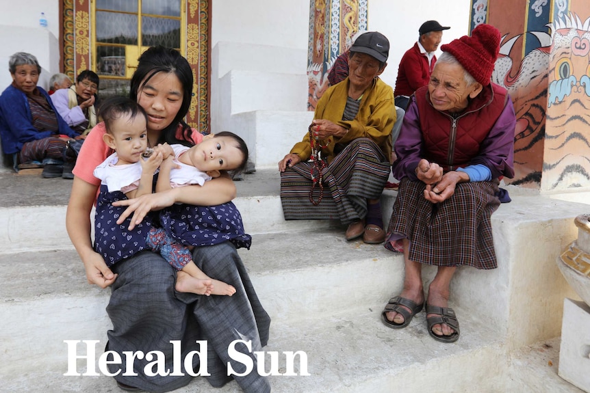 Mother Bhumchu Zangmo with Nima and Dawa sit outside a temple as older Bhutanese women gather around them.