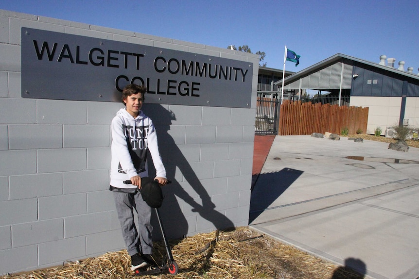 A young child holds a scooter in front of a community college sign