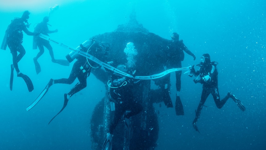 Divers swim near an artificial reef under water and cut a ribbon