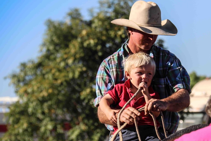 LANDLINE: A man and young boy ride a horse at the Borroloola rodeo