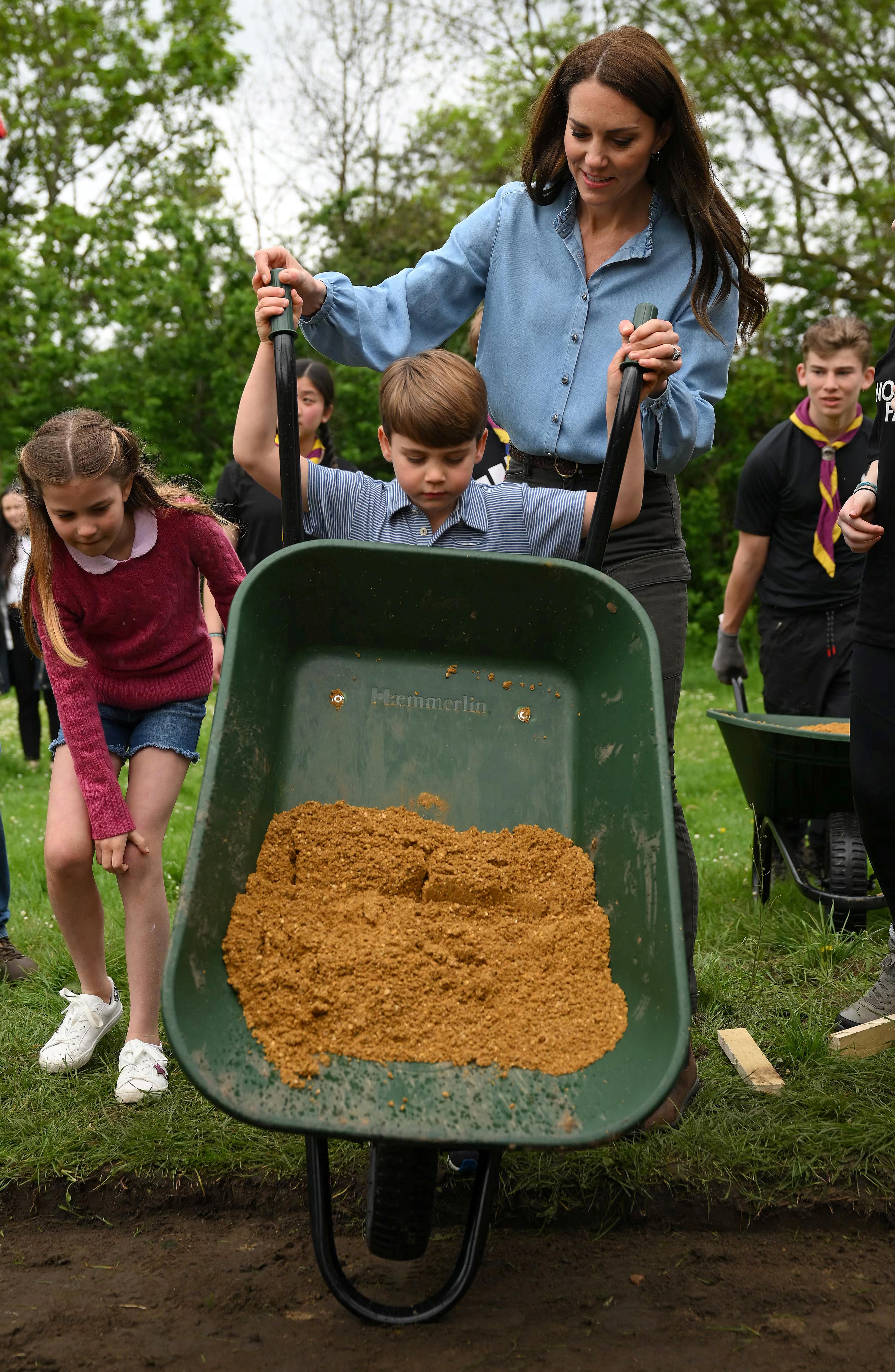 Kate helps her youngest son Louis tip dirt out of a wheelbarrow.