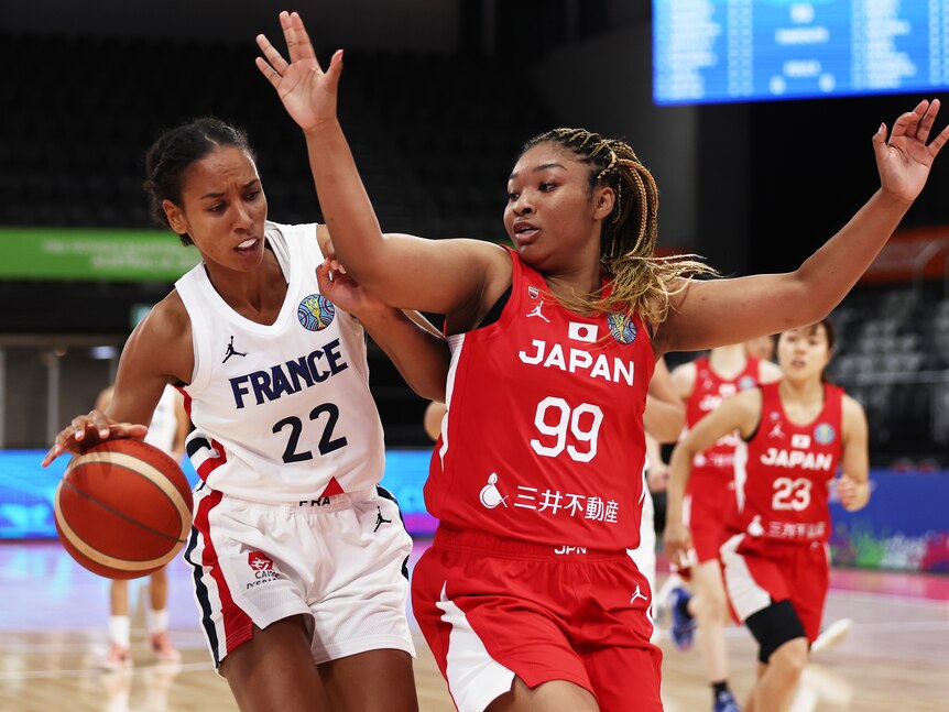 A French female basketballer tries to get around her Japanese opponent.