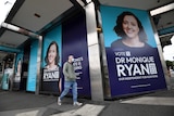 A man wearing a mask walks past large posters of Kooyong candidate Monique Ryan on a building.