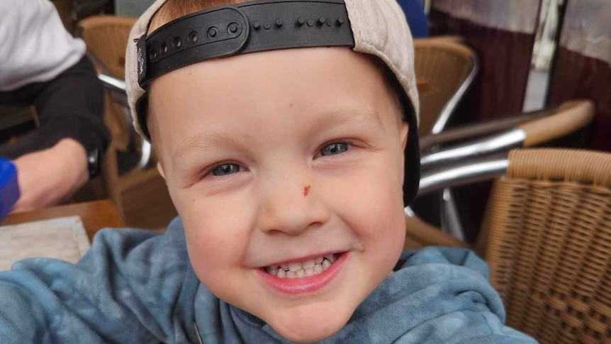 Chris, aged 3, smiles for a photo, wearing a cap backwards.