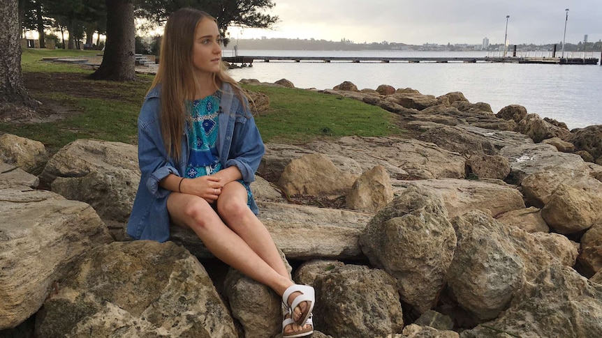 Grace Brandenburg sits on rocks on the foreshore looking out to sea.
