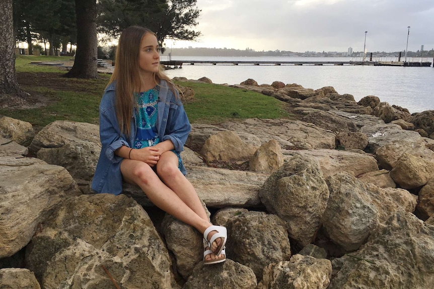 Grace Brandenburg sits on rocks on the foreshore looking out to sea.