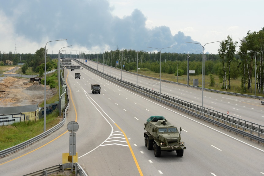 Four military vehicles drive along an empty highway
