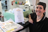 A woman in a black chef's cap and shirt standing at a cafe counter.