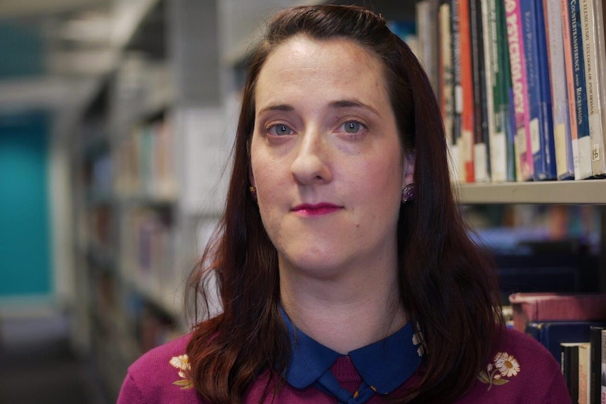 Close up shot of a woman with brown hair standing in front of a shelf of books