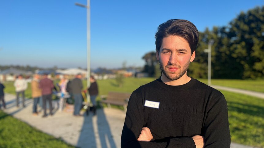 Brunette man looking into sun with crowd behind him in housing estate