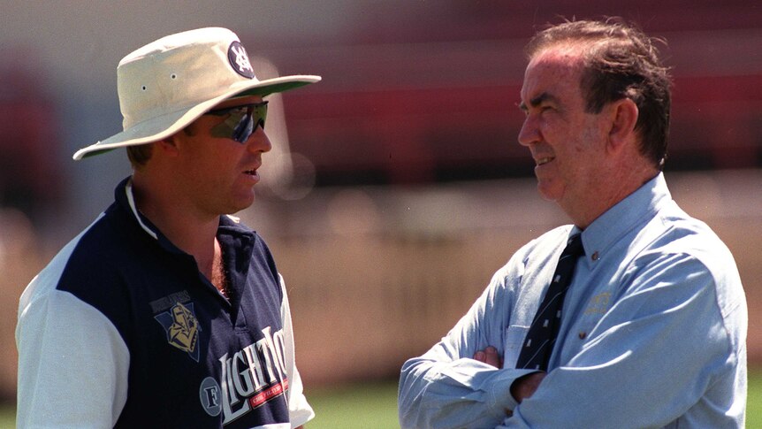 Two men discuss cricket tactics int he middle of a sports oval.