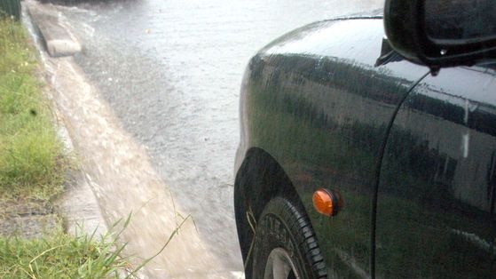 Water gushes down a gutter and sprays as it hits the tyre of a parked car after a torrential downpour in Brisbane on January 6, 2007.