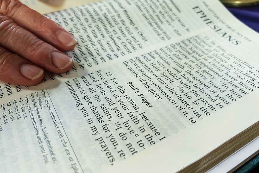 A close up image of an open bible with a hand pointing to a verse in Ephesians