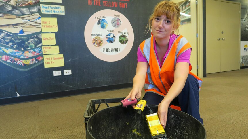 a woman holds a handful of discarded vapes from a bin wearing a high-vis vest