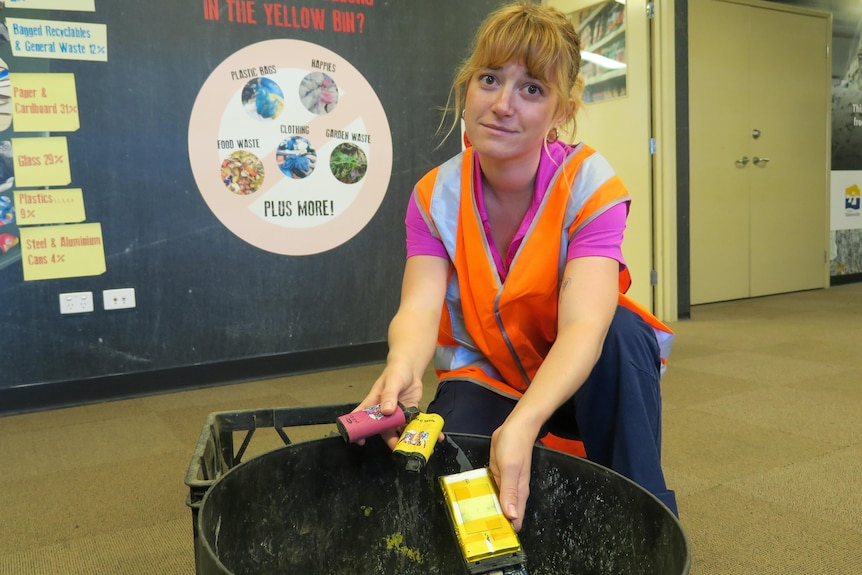 a woman holds a handful of discarded vapes from a bin wearing a high-vis vest