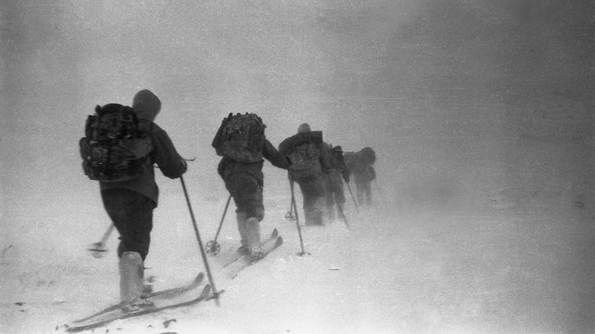 A black and white photo of a group of skiers in line heading into a storm 