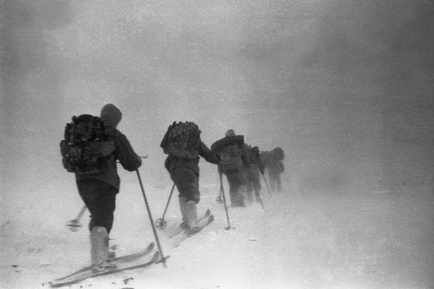 A black and white photo of a group of skiers in line heading into a storm 