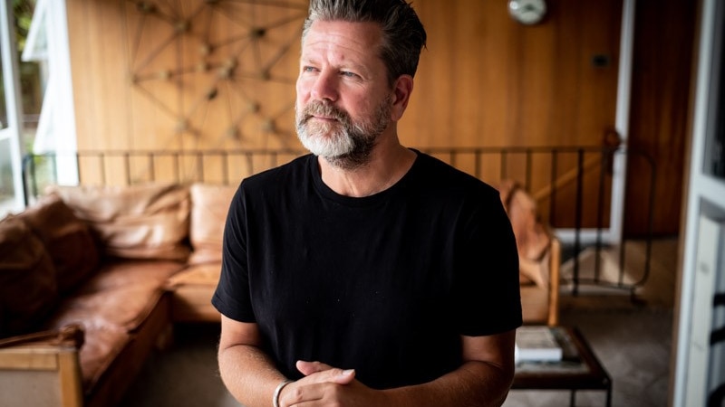 Tim 'Rosso' Ross wears a black shirt, standing in his mission brown living room