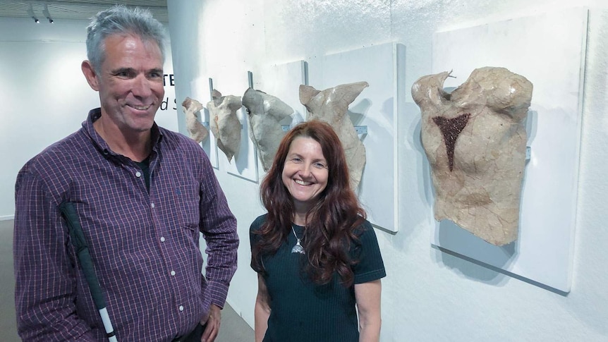 Blind art lover Geoff Munck, holding his cane, stands next to artist Katrin Terton in front of section of exhibition