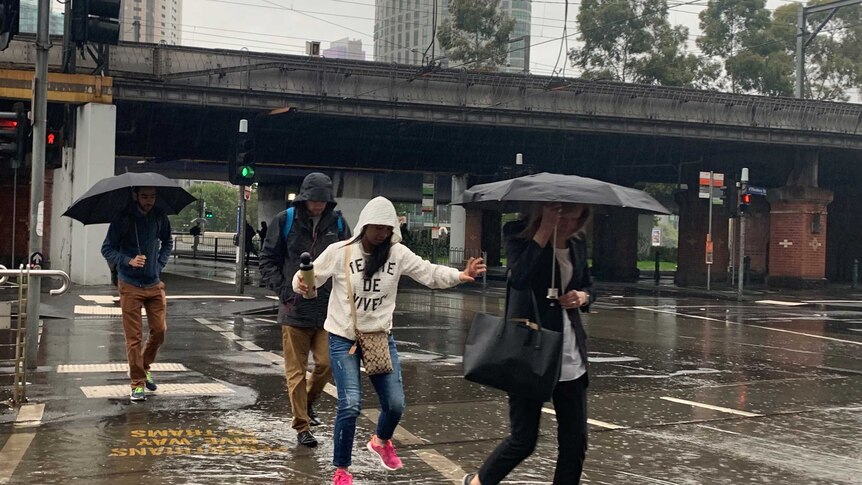 Pedestrians awkwardly jump over puddles as they cross Flinders Street in Melbourne's CBD.