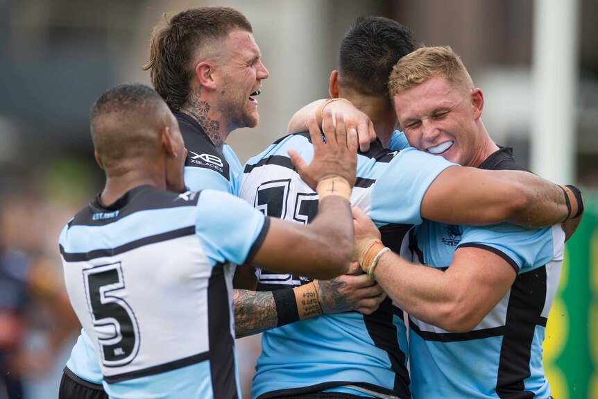 Briton Nikora is swamped by teammates as they celebrate a try for the Sharks against the Titans