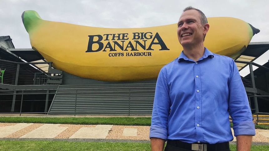 Man in blue collared shirt stands in front of the Big Banana - a big yellow house-sized banana.