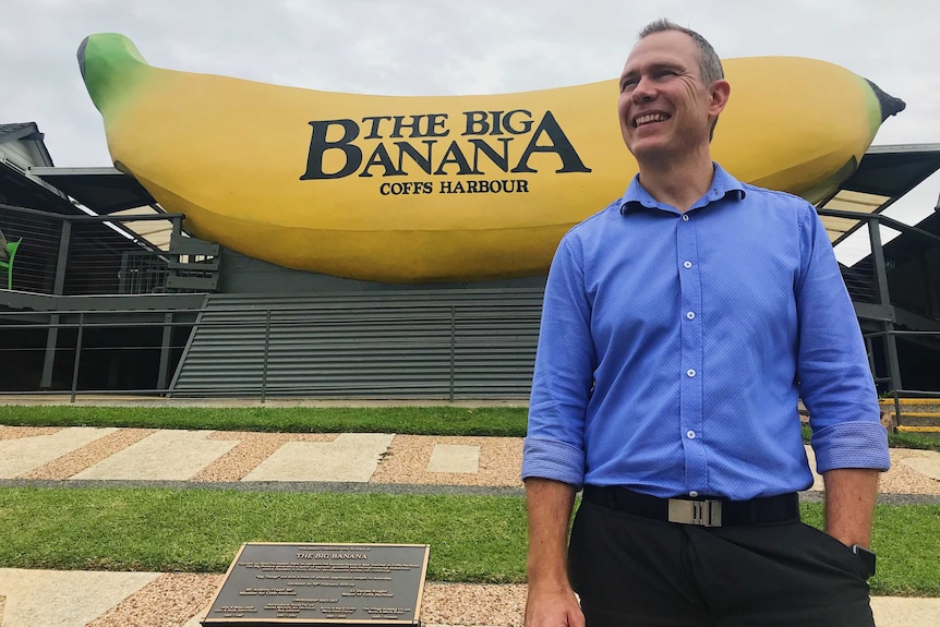 Man in blue collared shirt stands in front of the Big Banana - a big yellow house-sized banana.