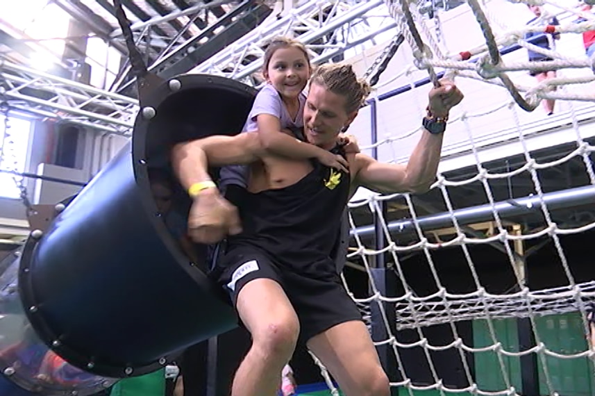 A girl gets a piggyback across an agility course in a gymnasium.