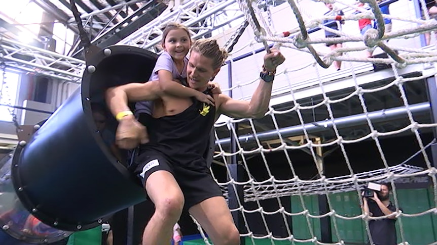 A girl gets a piggyback across an agility course in a gymnasium.