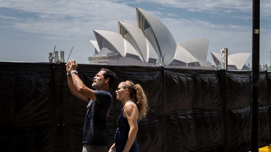 man and woman taking photo in front of a black fence with opera house in background
