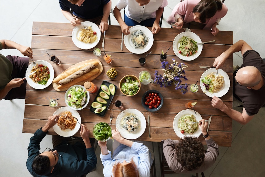 An aerial shot of a group of people sitting around a dining table full of food. 