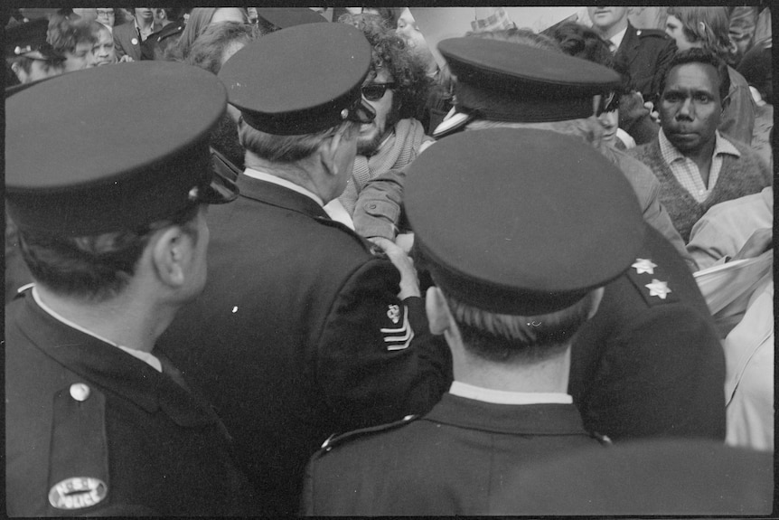 A black and white photo of a group of uniformed police officers looking towards a crowd of people.